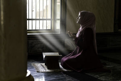 Side view of a young woman sitting by window