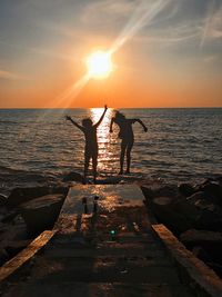 Silhouette people standing on beach against sky during sunset