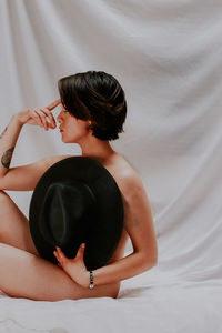 Side view of woman sitting on bed at home