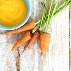 Close-up of carrots and its pure in bowl kept on wooden surface