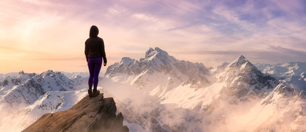 Rear view of person standing on snowcapped mountain against sky