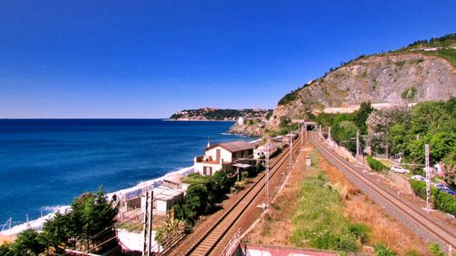 Road leading towards sea against clear blue sky