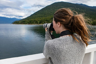 Rear view of woman photographing lake by mountains