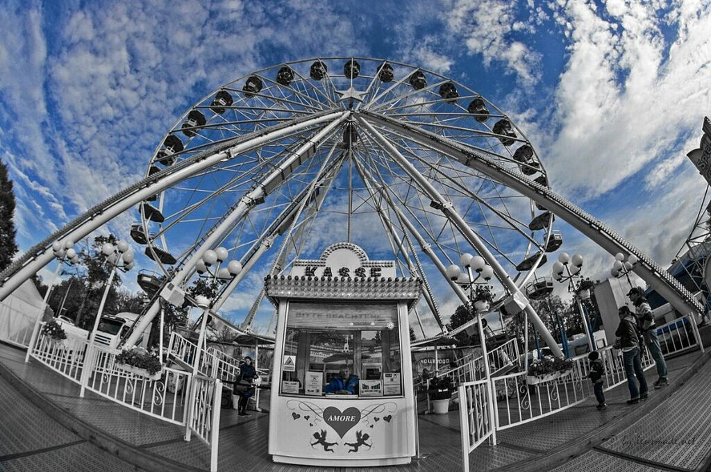 sky, amusement park, built structure, architecture, amusement park ride, arts culture and entertainment, cloud - sky, ferris wheel, low angle view, incidental people, building exterior, day, outdoors, cloud, leisure activity, railing, travel destinations, sunlight, metal, travel