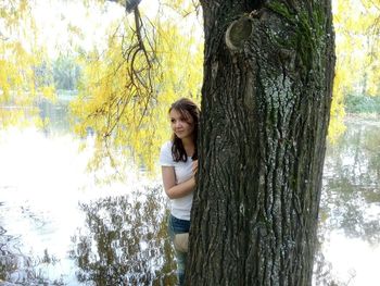 Thoughtful woman hiding behind tree by calm lake