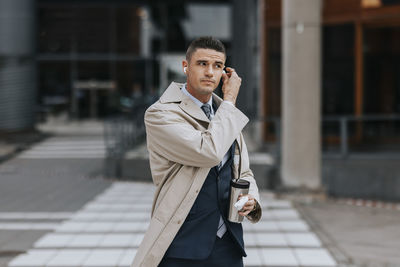 Businessman wearing wireless in-ear headphones while standing at street