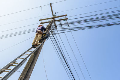 Low angle view of electrician repairing power lines against clear sky
