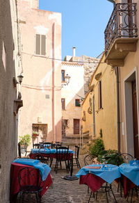 Empty chairs and tables in alley amidst buildings in city