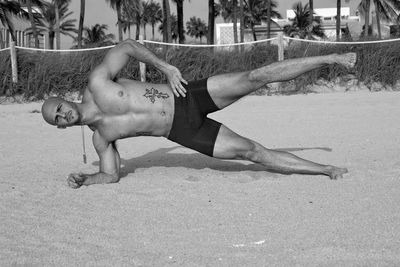 Full length of shirtless man on sand at beach