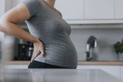 Mid section of pregnant woman standing in kitchen