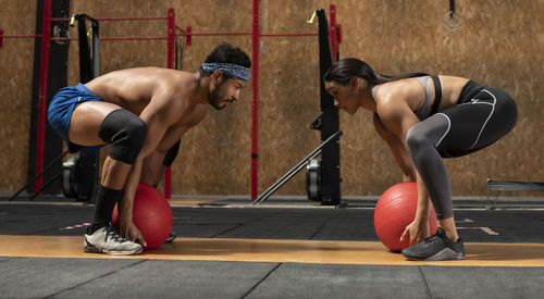 Concentrated sportswoman and sportsman doing squats with heavy medical balls during functional intense training in sports club