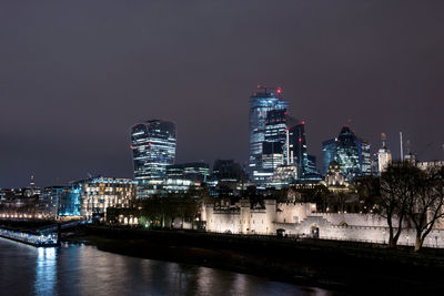 Illuminated buildings by river against sky at night