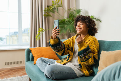 Young woman using mobile phone while sitting on sofa at home
