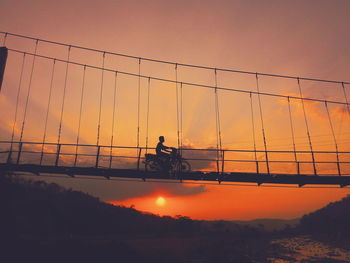 Low angle view of silhouette man riding motorcycle on bridge during sunset