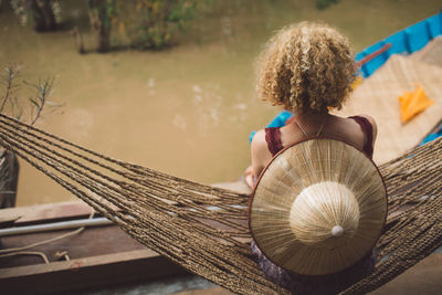 Rear view of woman with hat sitting on hammock