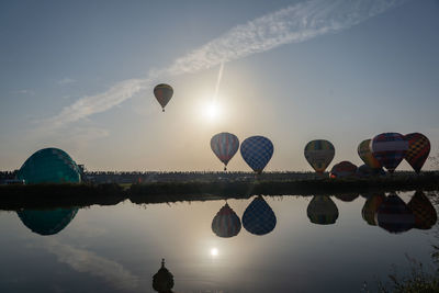 Reflection of hot air balloons in lake against sky during sunset