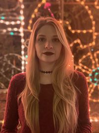 Portrait of beautiful young woman standing against illuminated lighting