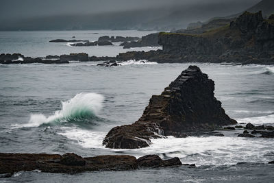 Waves breaking on rocks at shore against sky