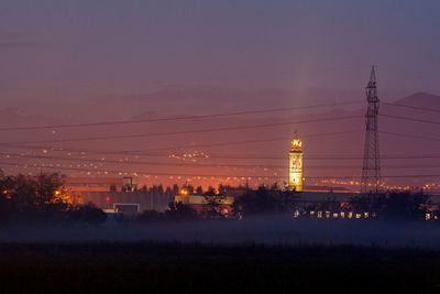 Silhouette trees and electricity pylon against sky at night
