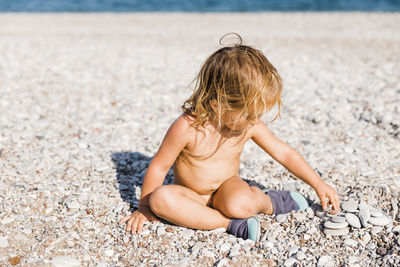 Full length of naked girl sitting on pebbles at beach