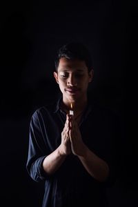 Man praying with lit candle against black background