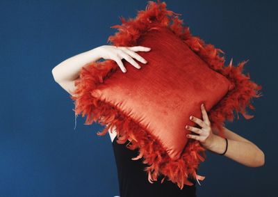 Woman holding brown pillow while standing against blue background