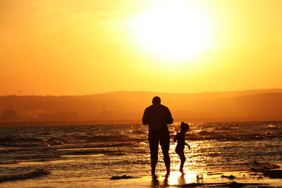 Silhouette men on beach against sky during sunset