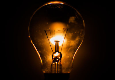 Close-up of illuminated light seen through bulb against black background