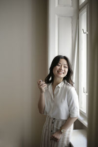 Smiling woman applying perfume while standing by window