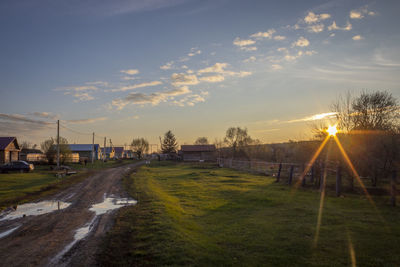 Road amidst field against sky during sunset