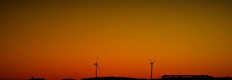 Silhouette of wind turbine against orange sky