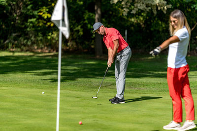 Young couple playing golf on a golf course, woman pointing to the golf hole