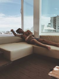 Woman lying down on window against sky