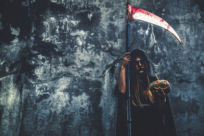 Woman in witch costume holding illuminated jack o lantern while standing against wall