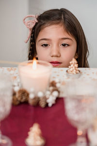 Tender child contemplating flaming candle in glass on table with coniferous cones during new year holiday at home