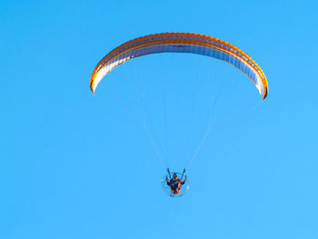 Low angle view of man paragliding against clear blue sky