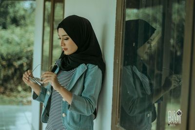 Young woman looking through window at home