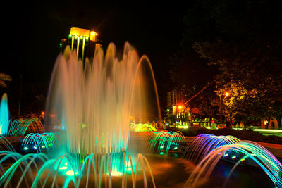 Light trails on fountain in city against sky at night