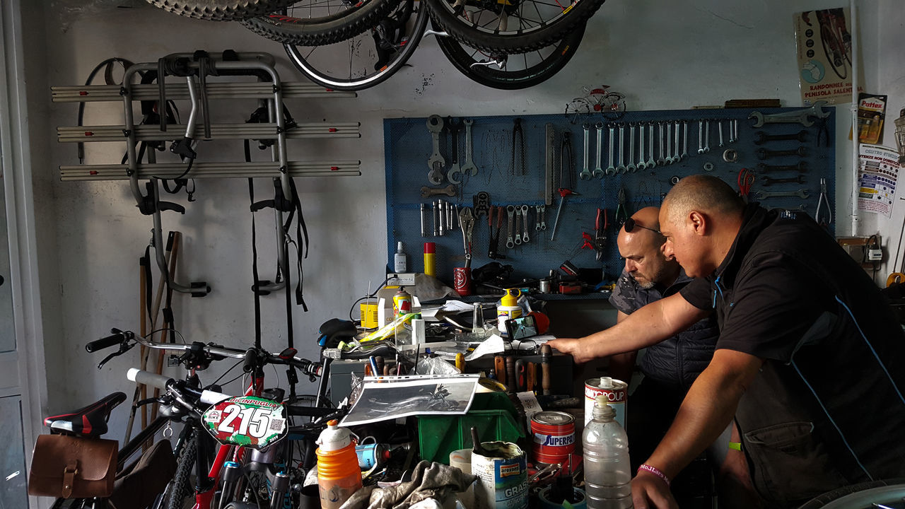 real people, occupation, men, one person, waist up, indoors, lifestyles, workshop, repairing, young adult, holding, working, adult, standing, bicycle, shopping, auto repair shop, transportation, mechanic, repair shop, garage