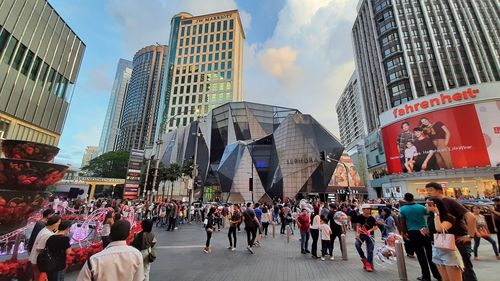 People walking on street amidst buildings in city against sky