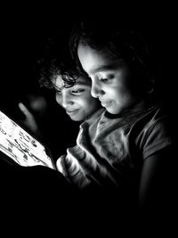 Smiling cute siblings playing on digital tablet in darkroom