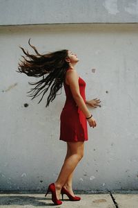 Side view of woman with tousled hair standing on footpath against wall