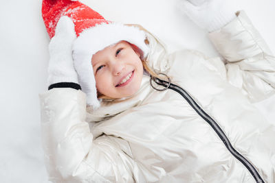 Portrait of cute girl wearing santa hat lying on snow covered land