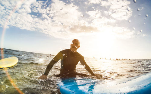 Man surfing in sea against sky during sunset