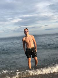 Full length of shirtless man standing in sea against sky