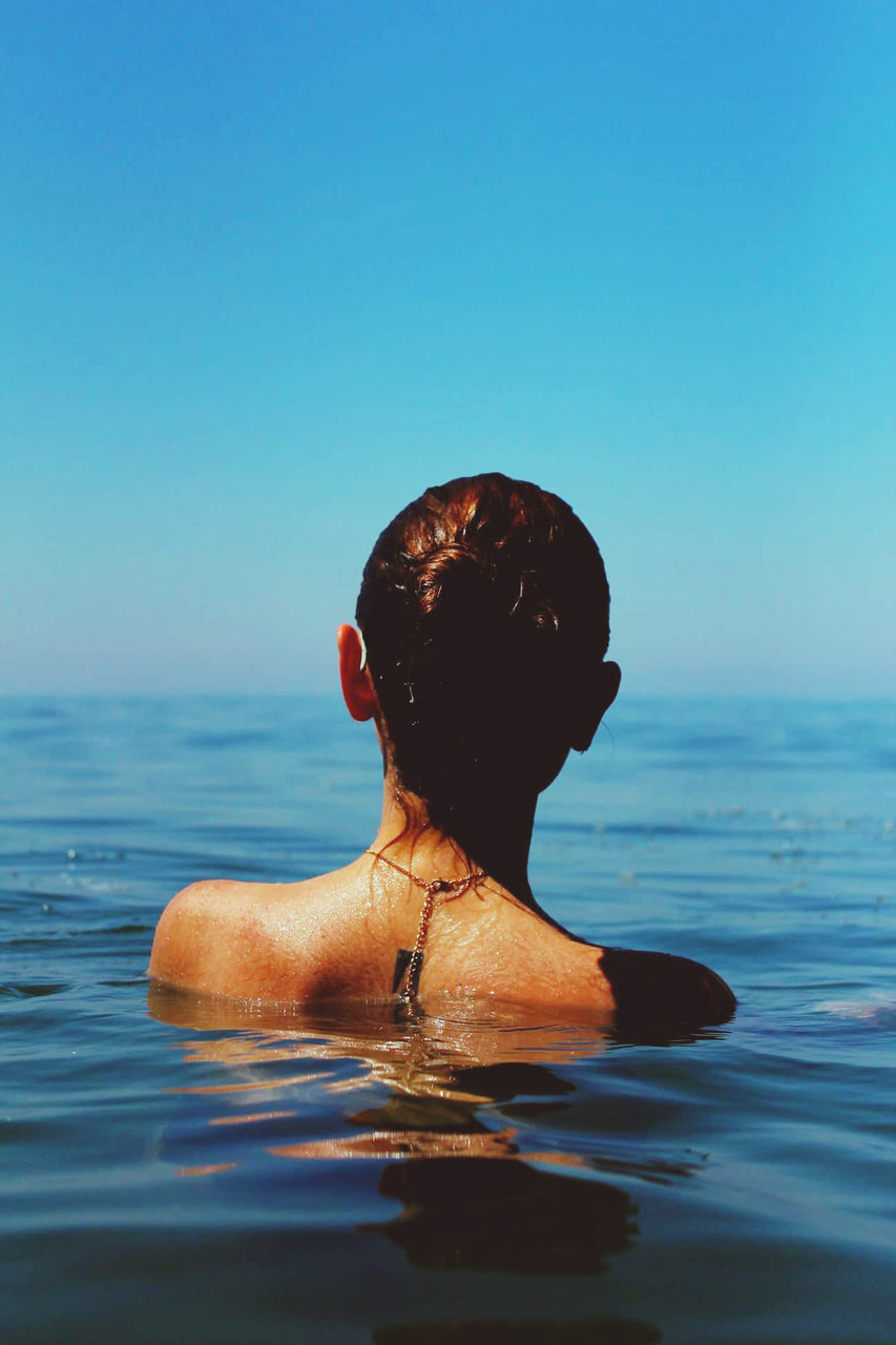 REAR VIEW OF MAN WITH ARMS RAISED IN SEA AGAINST SKY