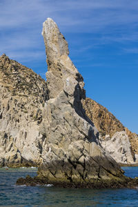 Rock formations on shore by sea against blue sky