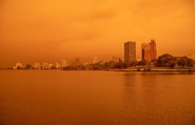 Sea by buildings against sky during sunset