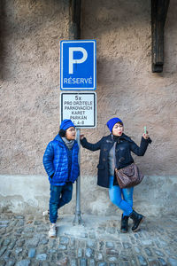 Mother with son taking selfie while standing by information sign against wall