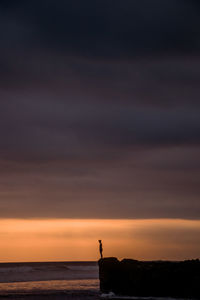 Silhouette person standing on rock against sea during sunset